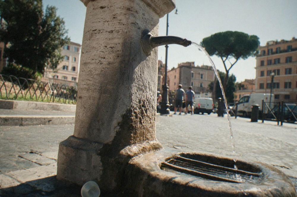 A stone drinking fountain with a curved spout running water onto a Roman street