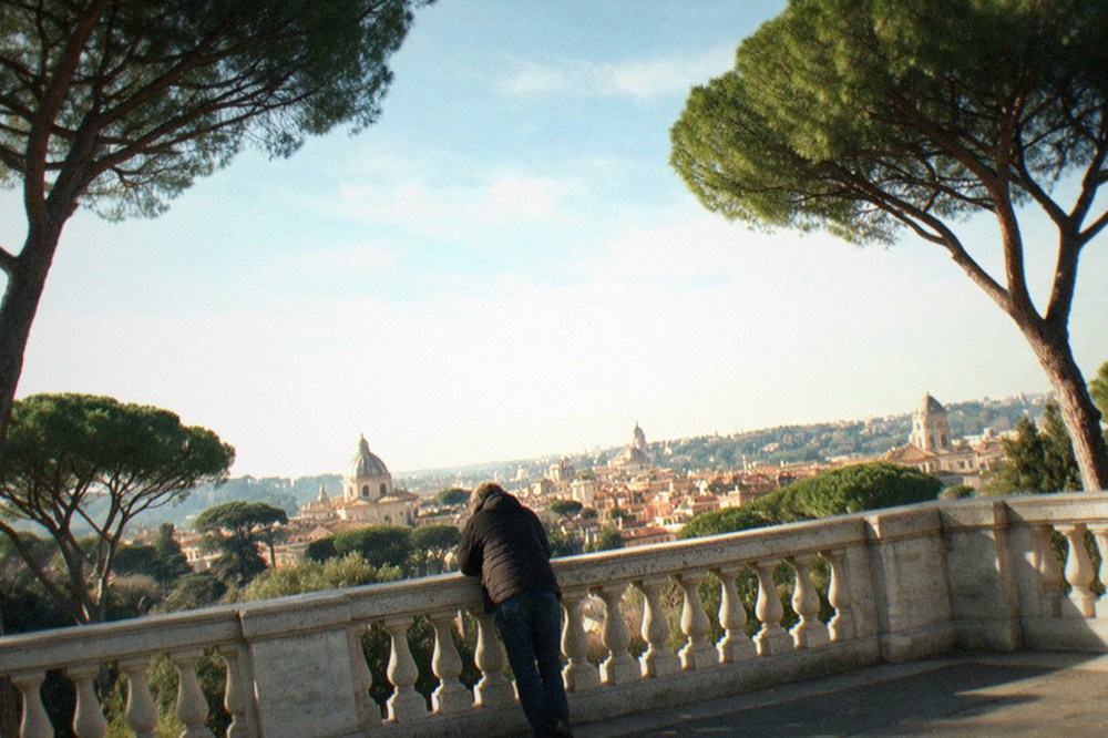 A tree-lined Rome terrace overlooking domes and rooftops in soft light