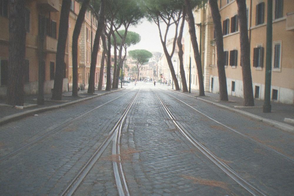 A Rome tram moving along a tree-lined street past old apartment buildings