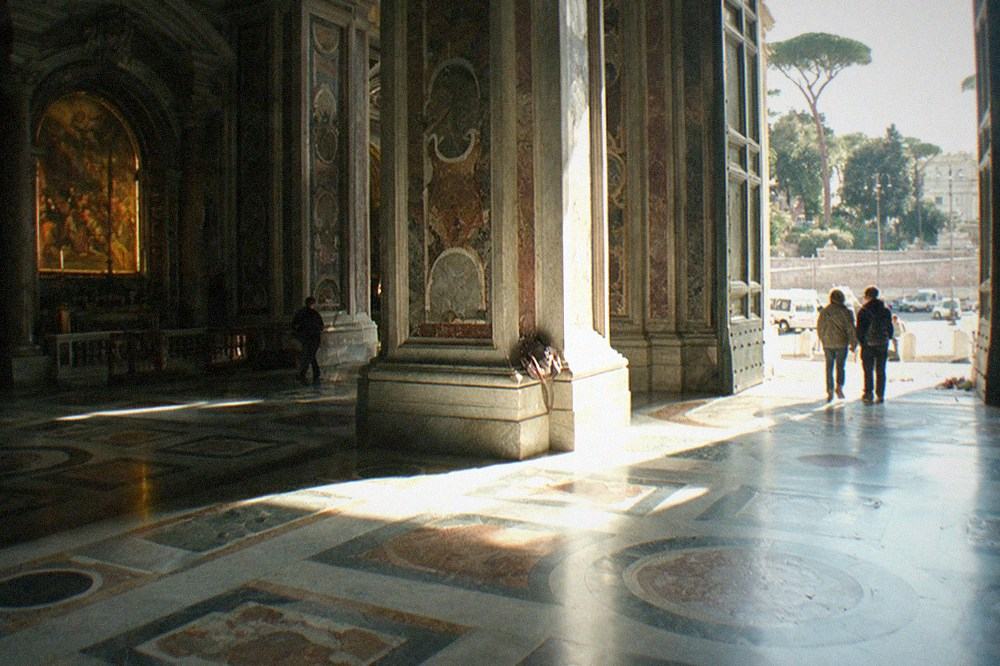 Sunlit basilica nave with paintings in side chapels and a patterned marble floor