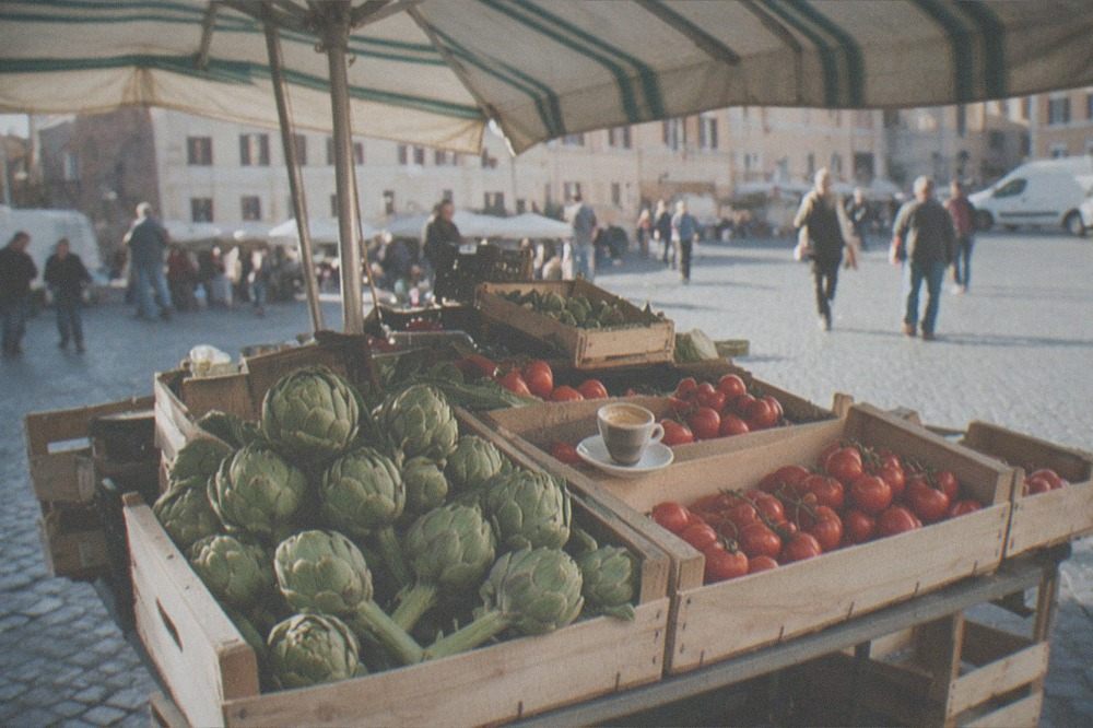 A Roman market stall with crates of vegetables and a striped canvas awning