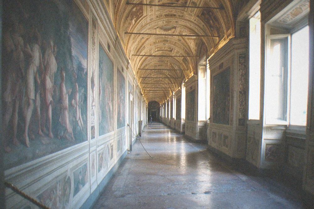 Long Vatican museum corridor with frescoed ceiling and marble floor stretching into the distance
