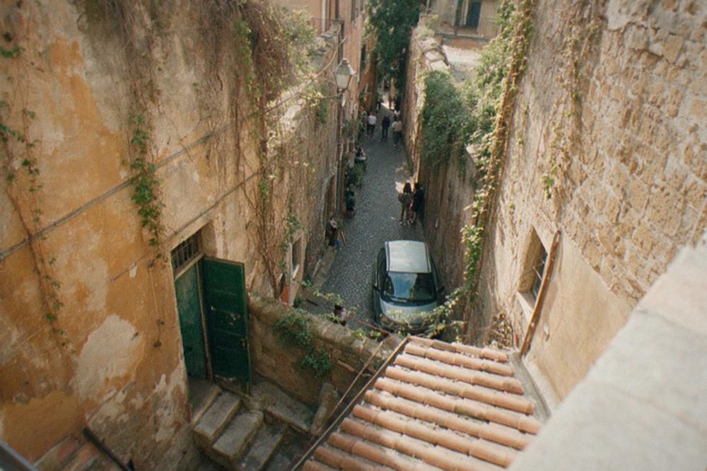 Sunlit Trastevere alley with hanging vines and worn stone walls