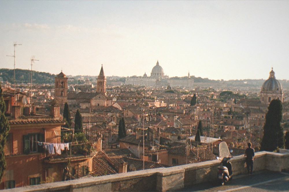 A wide view of Rome rooftops and domes seen from a hillside terrace in late afternoon light