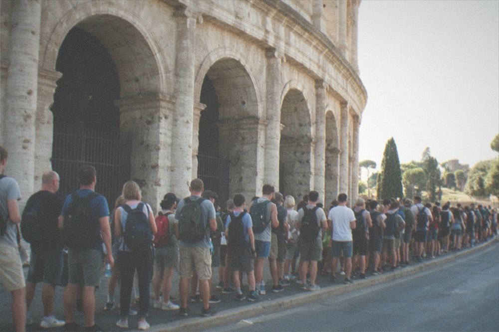 A queue of visitors stretching along the pavement beside the Colosseum arches