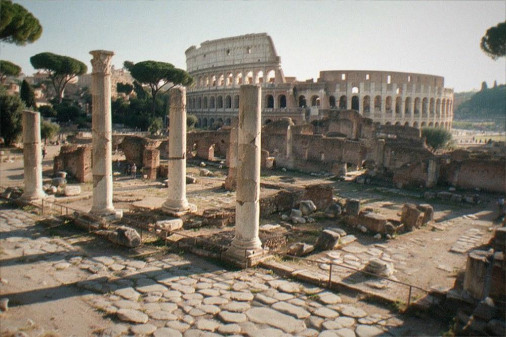 Stone columns and ruined walls of the Roman Forum with the Colosseum behind