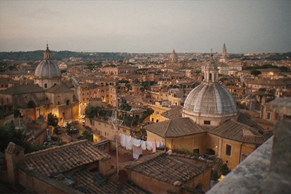 Rome rooftops and domes seen from a high terrace at dusk, with warm light on old buildings