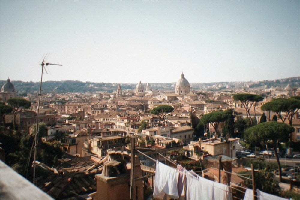 A wide Rome cityscape at golden hour with domes, rooftops and soft warm light